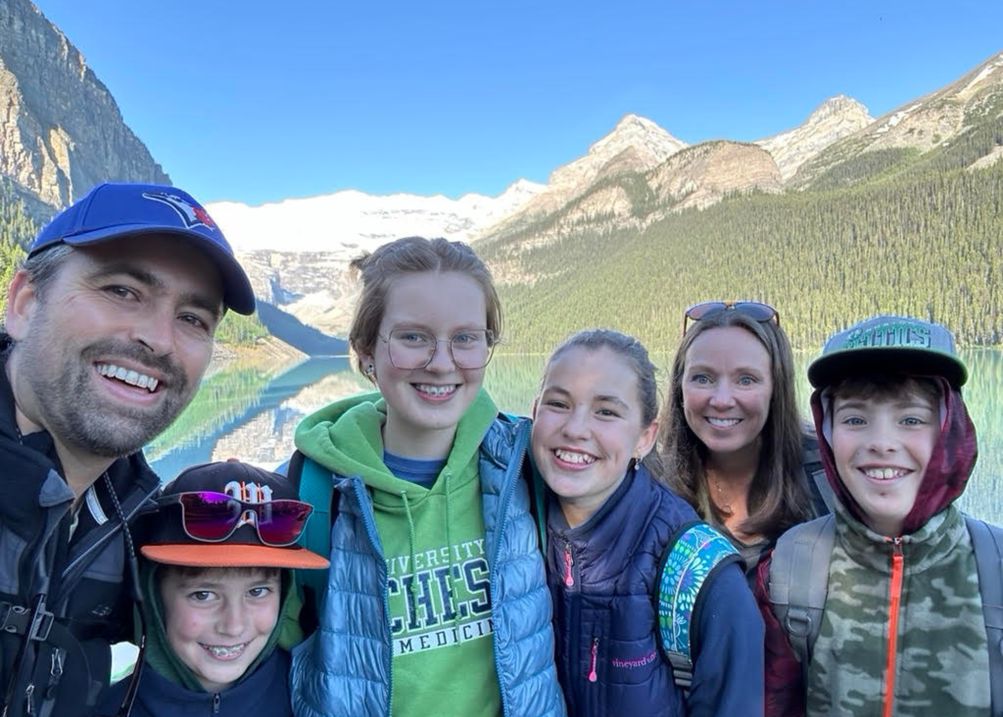 Tom Evans and Family on a hike Family of six including Tom Evans and his wife Christina with their 4 children on a hike smiling in front of a bright blue lake in the mountains,